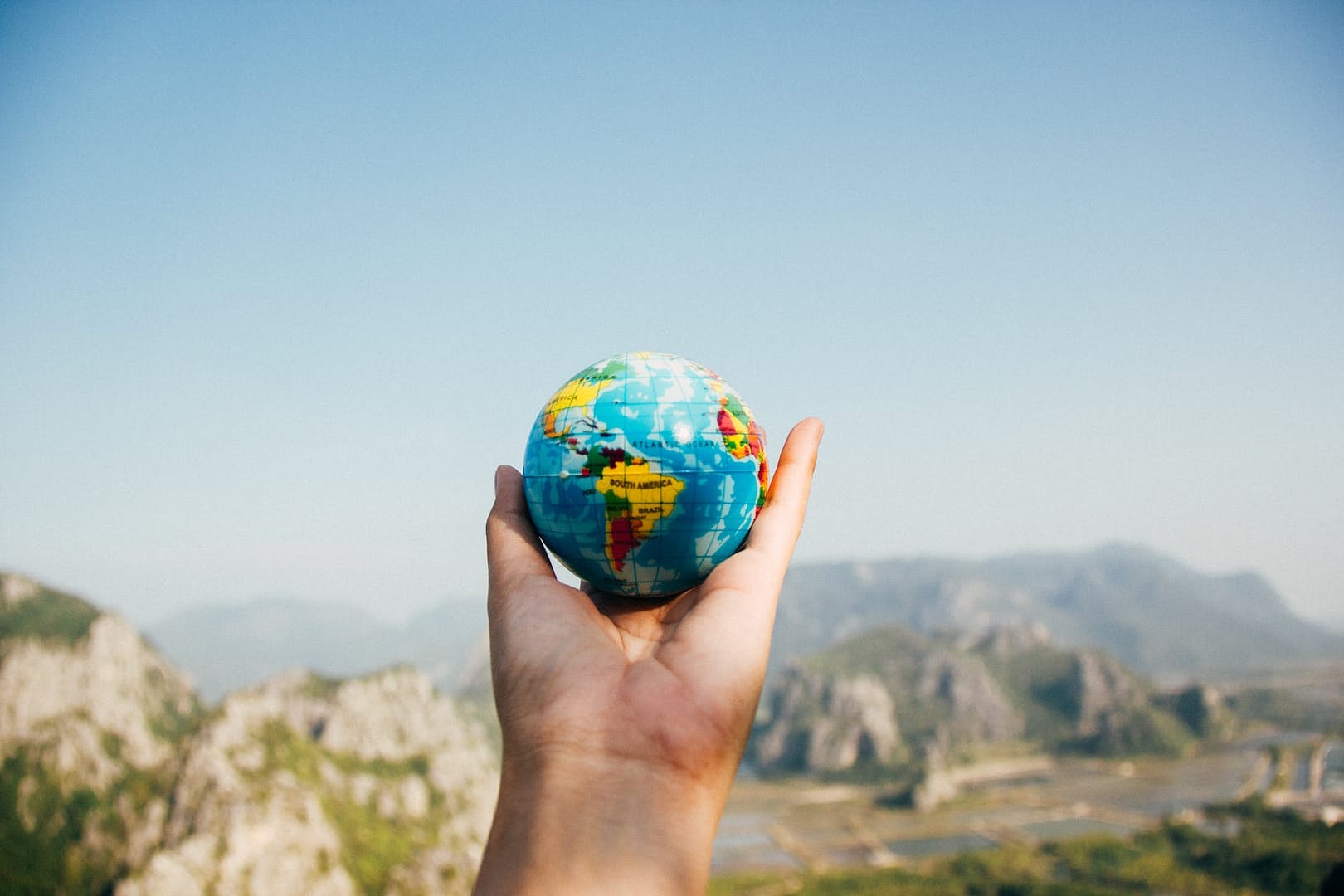 Earth person holding world globe facing mountain